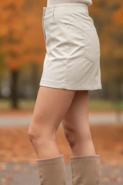 Falda corta de efecto piel, fit ajustado, cintura alta, costuras frontales decorativas, bolsillos delanteros y traseros de parche. Cierre frontal con cremallera oculta.