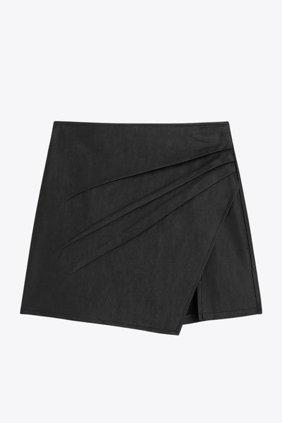 Falda short corto de efecto piel, cintura alta, corte en a, cruce frontal con abertura y plisados laterales. Cierre lateral con cremallera oculta.