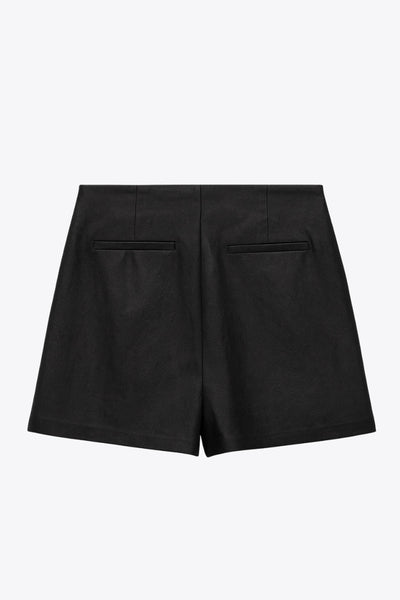 Falda short corto de efecto piel, cintura alta, corte en a, cruce frontal con abertura y plisados laterales. Cierre lateral con cremallera oculta.