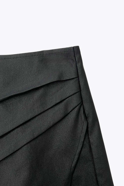 Falda short corto de efecto piel, cintura alta, corte en a, cruce frontal con abertura y plisados laterales. Cierre lateral con cremallera oculta.