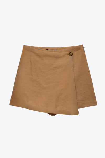 Falda short corto de cintura alta, corte en a, cruce frontal con abertura en bajo y botón en contraste. Cierre lateral con cremallera oculta.