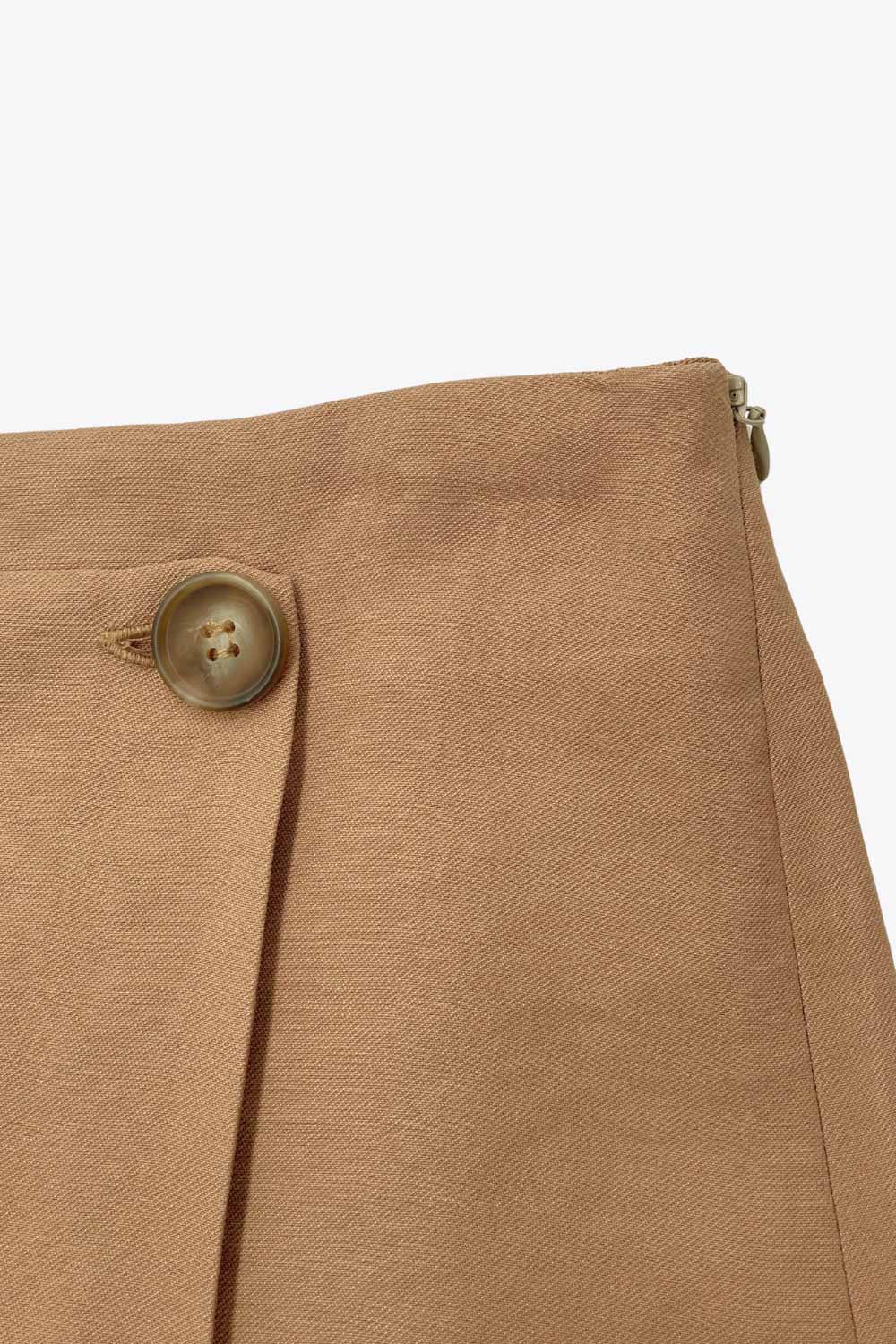 Falda short corto de cintura alta, corte en a, cruce frontal con abertura en bajo y botón en contraste. Cierre lateral con cremallera oculta.