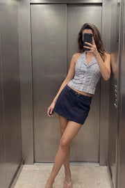 Falda short corto de fit recto, cintura alta con pretina y trabillas, vivos decorativos posteriores, cierre frontal con broche y cremallera ocultos. Detalle de cinturón en contraste con hebilla.