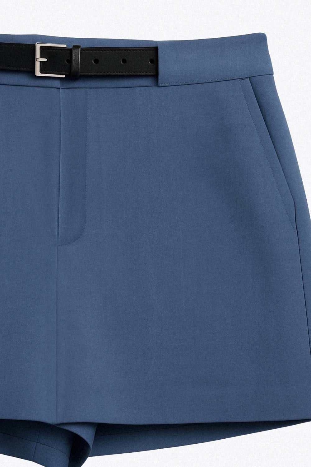 Falda short corto de fit recto, cintura alta con pretina y trabillas, vivos decorativos posteriores, cierre frontal con broche y cremallera ocultos. Detalle de cinturón en contraste con hebilla.