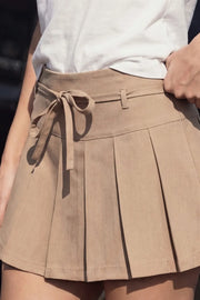 Falda short corto tableado, de corte en a, cintura alta con pretina, trabillas y lazo amarrable del tejido. Detalle de tableado en bajo y cierre lateral con cremallera oculta.