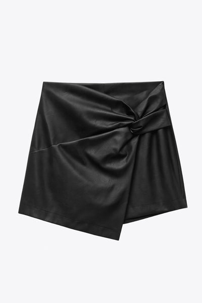 Falda short corto de efecto piel, fit ajustado, cintura alta, cruce frontal asimétrico con nudo y plisados decorativos frontales. Cierre posterior con cremallera oculta.