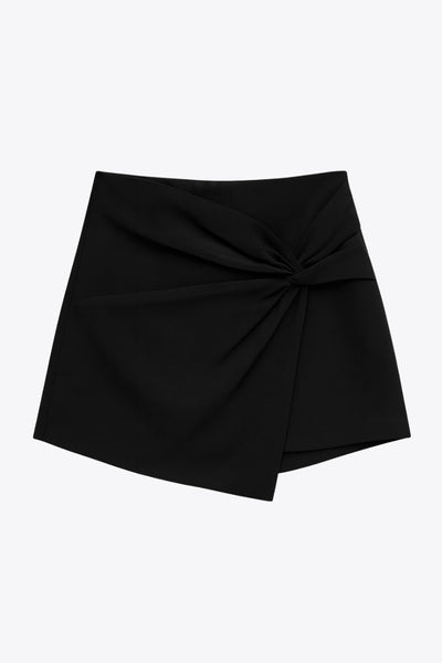 Falda short corto de fit ajustado, cintura alta, cruce frontal con nudo y plisados decorativos frontales. Cierre posterior con cremallera oculta.