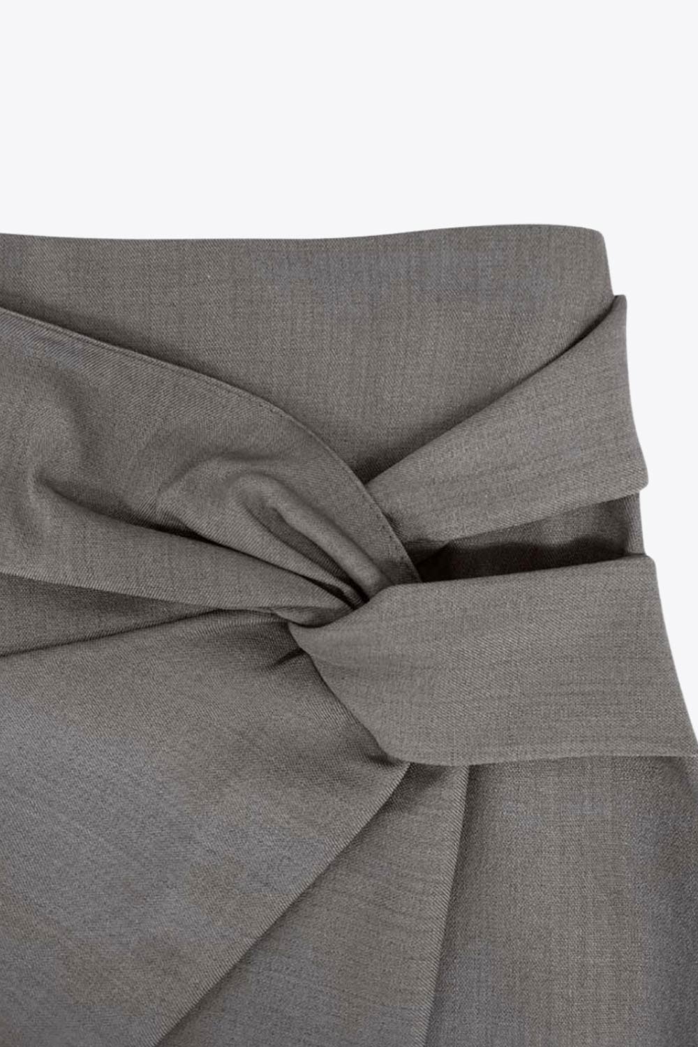 Falda short corto de fit ajustado, cintura alta, cruce frontal con nudo y plisados decorativos frontales. Cierre posterior con cremallera oculta.