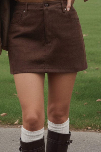 Falda short corto de gamuza, fit ajustado, cintura alta con pretina y trabillas, bolsillos delanteros, cierre frontal con botón y cremallera oculta.