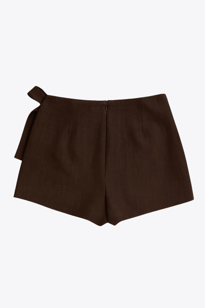 Falda short corto de cintura alta, corte en a, sobrefalda con cruce frontal, lazo lateral amarrable y cierre posterior con cremallera oculta.