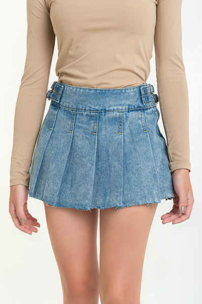 Falda short corto tableado de denim, cintura media con pretina ancha, trabillas laterales decorativas con hebillas en contraste y cierre lateral con cremallera oculta. Detalle de rotos en bajo.