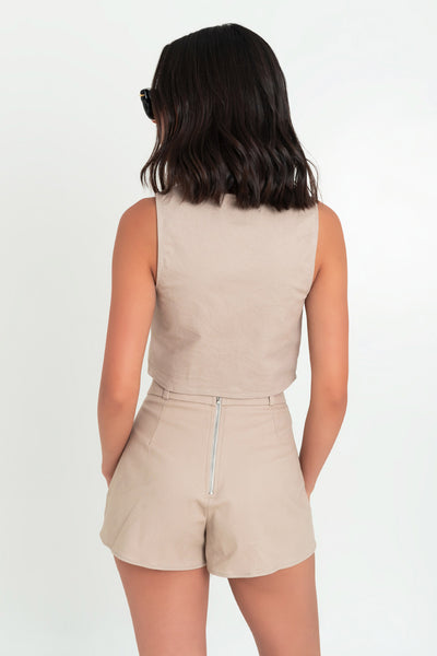 Falda short corto de cintura alta con pretina y trabillas, corte en a, cruce frontal con bajo asimétrico y cierre posterior con cremallera visible en contraste.