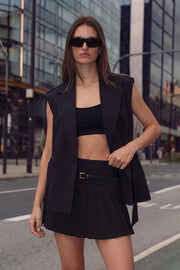 Falda short corto de cintura alta, corte en a, tableado en bajo, pretina ancha, trabillas y cinturón con hebilla en contraste. Cierre lateral con cremallera oculta.