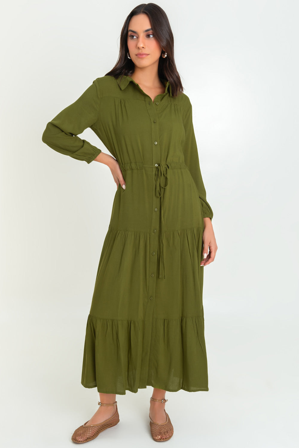 Maxi vestido camisero de fit recto, manga larga con rib elástico en puños, cuello camisero, plisados frontales, capas de olanes en bajo, jareta ajustable en cintura y cierre frontal con hilera de botones en contraste.