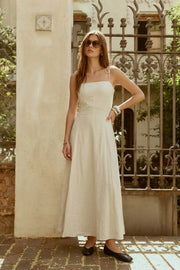 Vestido largo de fit ajustado, corte en a con olanes en bajo, tirantes delgados con nudo amarrable, escote recto y cierre posterior con cremallera oculta.