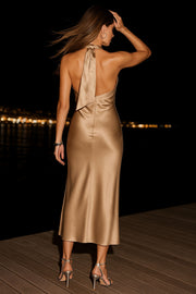 Maxi vestido satinado de fit recto, cuello halter cruzado con lazo amarrable posterior, escote en espalda y cierre posterior con cremallera oculta. Detalle de abertura lateral en bajo.
