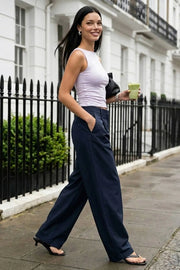 Pantalón de fit wide leg, pinzas frontales, cintura alta con pretina y trabillas, bolsillos delanteros y vivos decorativos traseros. Cierre frontal con broche y cremallera ocultos.