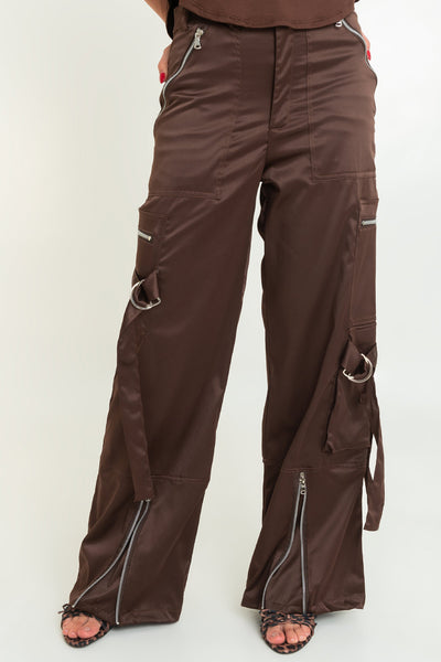 Pantalón satinado de cintura alta, fit wide leg, bolsillos delanteros y traseros de parche. Detalle de abertura frontal en bajo con cremalleras, bolsillos laterales cargo con cremalleras, trabillas y cartera. Cierre frontal con botón y cremallera oculta.