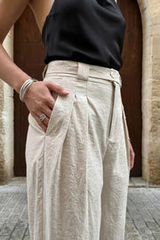 Pantalón de fit balloon, pinzas frontales, cintura alta con pretina, trabillas y cinturón del mismo tejido con ojales, bolsillos delanteros y vivos decorativos posteriores. Detalle de plisados en bajo con botones laterales y trabilla larga en cintura. Cierre frontal con botón y cremallera oculta.