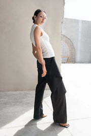 Pantalón recto de cintura alta con pretina, detalle de sobrefalda cruzada decorativa con bajo asimétrico, trabilla lateral, vivo decorativo posterior, cierre frontal con broche y cremallera ocultos.
