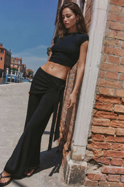 Pantalón fluido de fit wide leg, cintura media con pretina elástica, plisados en costado y detalle de pareo decorativo con nudo lateral.
