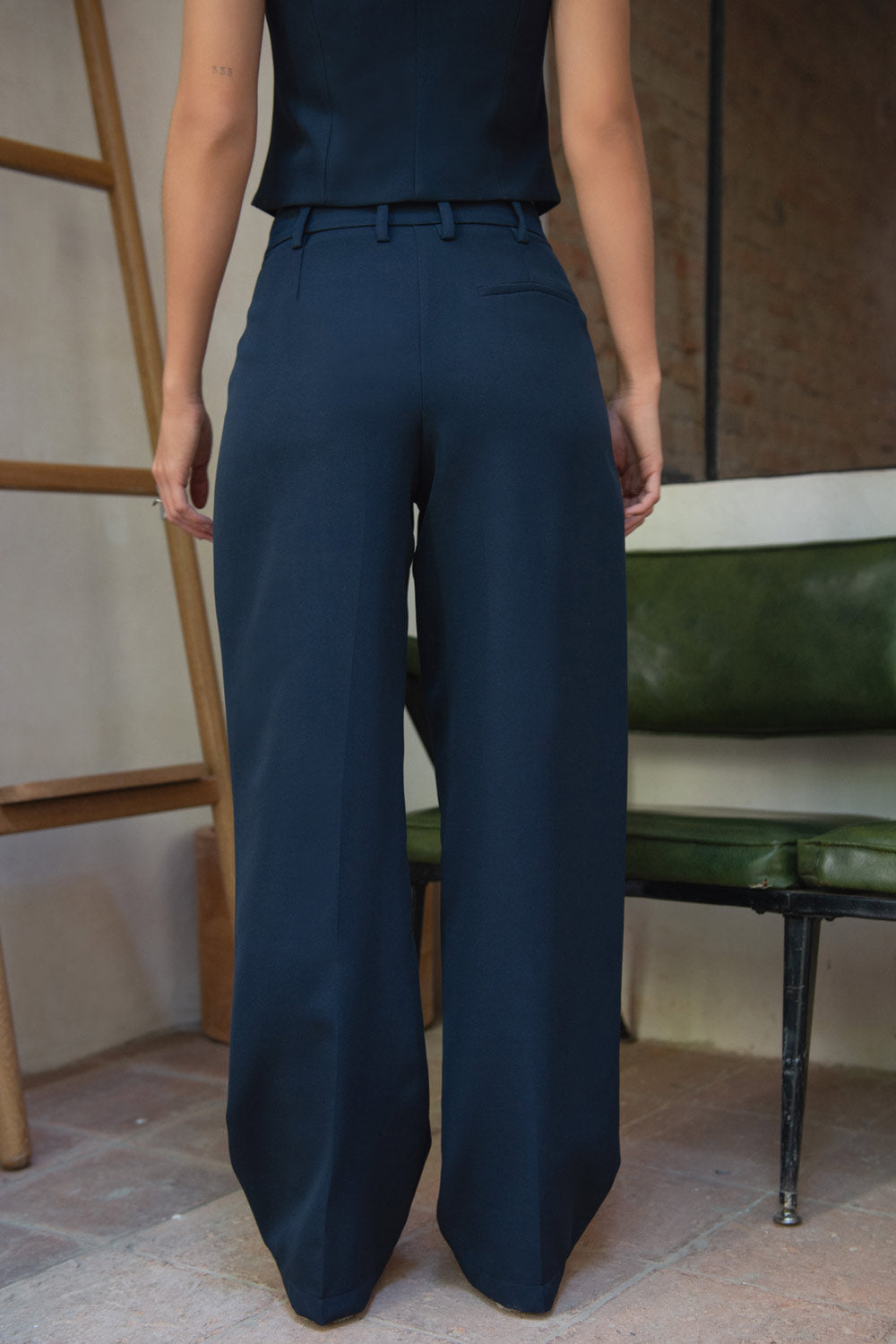 Pantalón de fit wide leg, cintura alta con pretina y trabillas, pinzas frontales, bolsillos delanteros, vivo decorativo posterior, cierre frontal con cremallera oculta y botón forrado. Detalle de raya frontal y posterior.