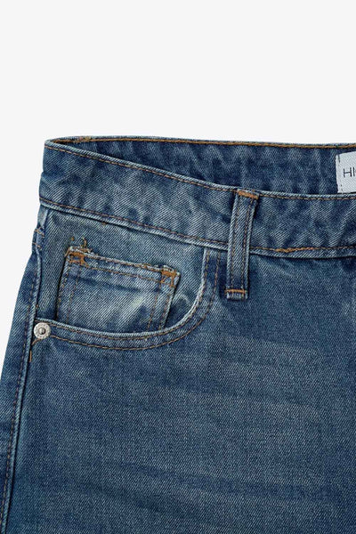 Pantalón de denim, fit recto, cintura alta con pretina y trabillas, detalle de rotos en bajo, bolsillos delanteros y traseros de parche. Cierre frontal con botón y cremallera oculta.