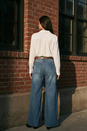 Pantalón de denim, fit wide leg, tiro medio con pretina y trabillas, bolsillos delanteros y traseros de parche. Cierre con botón y cremallera oculta. Detalle de costuras decorativas frontales.