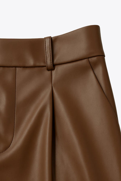 Pantalón de efecto piel, fit recto, cintura alta con pretina y trabillas, pinzas frontales, bolsillos delanteos y vivos decorativos posteriores.