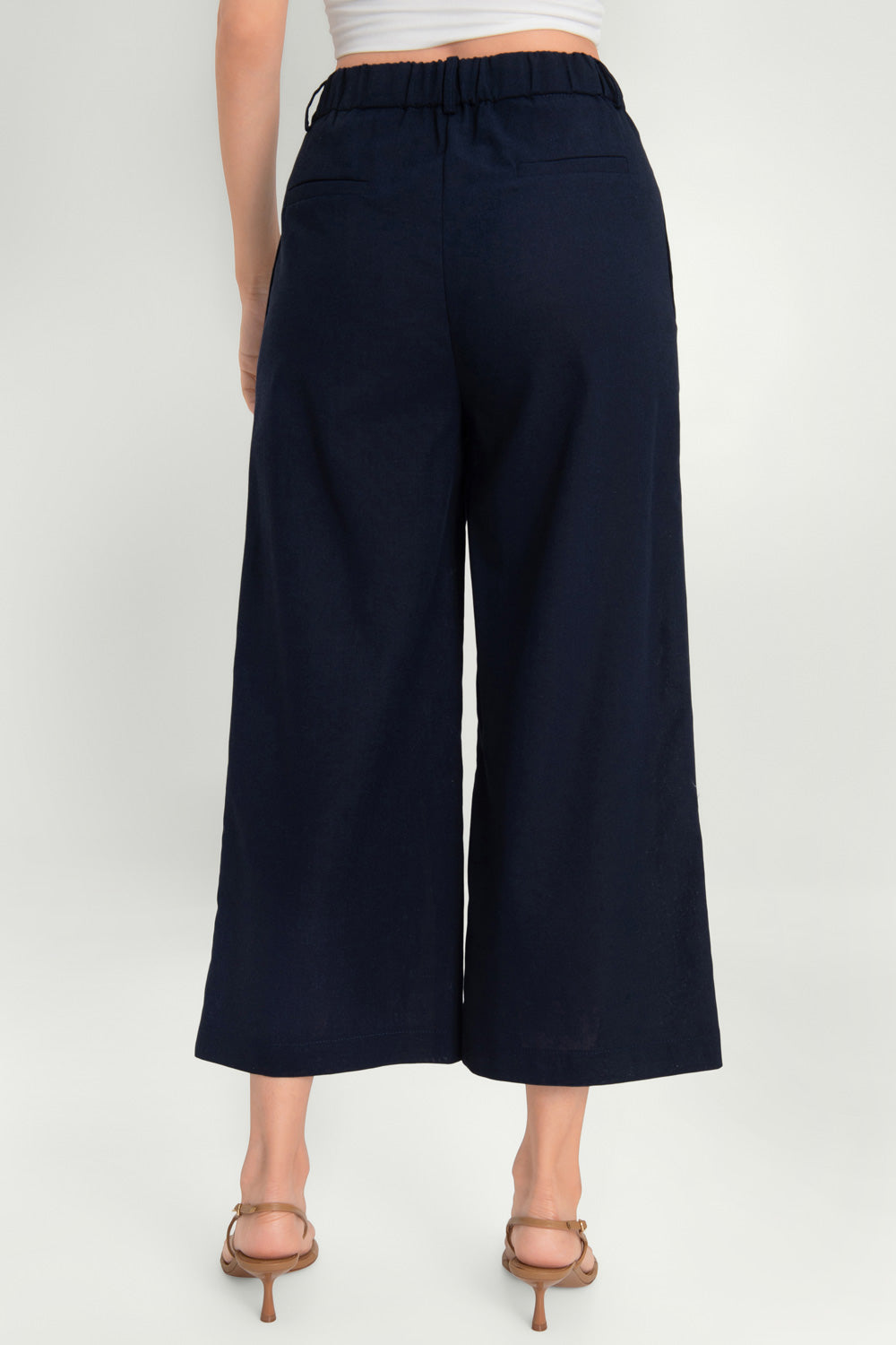 Pantalón de fit culotte, cintura alta con pretina elástica posterior y trabillas, pinzas frontales, bolsillos delanteros y vivos decorativos posteriores. Cierre frontal con cremallera oculta y trabilla con botón.