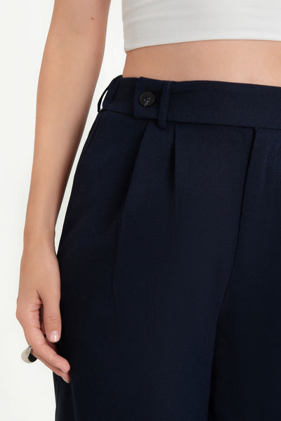 Pantalón de fit culotte, cintura alta con pretina elástica posterior y trabillas, pinzas frontales, bolsillos delanteros y vivos decorativos posteriores. Cierre frontal con cremallera oculta y trabilla con botón.