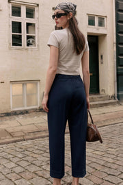 Pantalón de fit recto, cintura alta con pretina elástica posterior, pinzas frontales, bolsillos delanteros, vivo decorativo posterior y doblez en bajo. Cierre frontal con broche y cremallera ocultos.