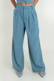 Pantalón de fit wide leg, cintura alta con pretina y trabillas, bolsillos delanteros y pinzas frontales. Cierre frontal con broche y cremallera oculta.