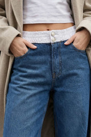 Pantalón wide leg de denim, cintura alta con pretina elástica en constraste, bolsillos delanteros y posteriores de parche. Cierre frontal con botones y cremallera oculta.