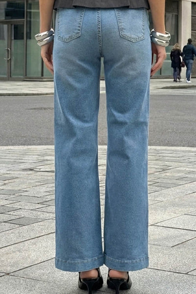 Pantalón de denim, fit recto, cintura alta con pretina y trabillas, bolsillos delanteros y traseros de parche. Cierre con botón y cremallera oculta.