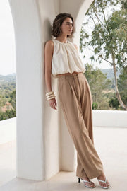 Pantalón de fit wide leg, cintura alta con pretina, trabillas y doble lazo amarrable, pinzas frontales y bolsillos delanteros. Cierre frontal con broche y cremallera ocultos.