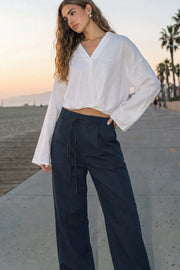 Pantalón de fit wide leg, cintura alta con pretina, trabillas y doble lazo amarrable, pinzas frontales y bolsillos delanteros. Cierre frontal con broche y cremallera ocultos.