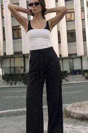 Pantalón de fit wide leg, cintura alta con pretina, trabillas y doble lazo amarrable, pinzas frontales y bolsillos delanteros. Cierre frontal con broche y cremallera ocultos.