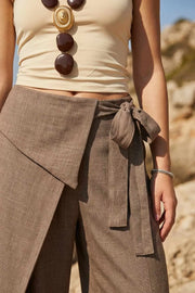 Pantalón de fit wide leg, bolsillos delanteros, cintura alta y cruce frontal con lazo amarrable lateral. Detalle decorativo en pretina frontal.