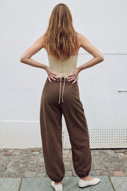 Pantalón de gamuza, fit balloon, pinzas frontales, cintura media con pretina elástica posterior, bolsillos delanteros y rib elástico en bajo. Cierre frontal con botón y cremallera oculta.