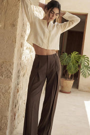 Pantalón de fit wide leg, cintura alta con pretina y trabillas, pinzas frontales, bolsillos delanteros, vivos decorativos posteriores, cierre frontal con broche y cremallera ocultos. Detalle de trabillas laterales ajustables en cintura.