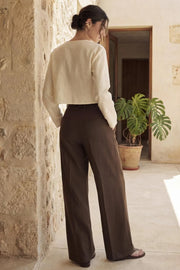 Pantalón de fit wide leg, cintura alta con pretina y trabillas, pinzas frontales, bolsillos delanteros, vivos decorativos posteriores, cierre frontal con broche y cremallera ocultos. Detalle de trabillas laterales ajustables en cintura.