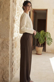 Pantalón de fit wide leg, cintura alta con pretina y trabillas, pinzas frontales, bolsillos delanteros, vivos decorativos posteriores, cierre frontal con broche y cremallera ocultos. Detalle de trabillas laterales ajustables en cintura.