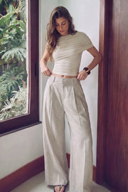 Pantalón de fit wide leg, cintura alta con pretina y trabillas, pinzas frontales, bolsillos delanteros, vivos decorativos posteriores, cierre frontal con broche y cremallera ocultos. Detalle de trabillas laterales ajustables en cintura con botones en contraste.