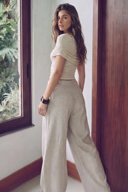 Pantalón de fit wide leg, cintura alta con pretina y trabillas, pinzas frontales, bolsillos delanteros, vivos decorativos posteriores, cierre frontal con broche y cremallera ocultos. Detalle de trabillas laterales ajustables en cintura con botones en contraste.