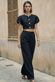 Pantalón de fit wide leg, cintura alta con pretina con detalle v posterior y trabillas, pinzas frontales, bolsillos delanteros, vivos decorativos posteriores, cierre frontal con botón en contraste y cremallera oculta.