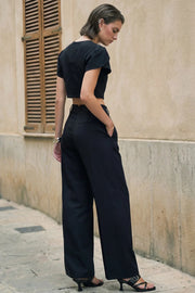 Pantalón de fit wide leg, cintura alta con pretina con detalle v posterior y trabillas, pinzas frontales, bolsillos delanteros, vivos decorativos posteriores, cierre frontal con botón en contraste y cremallera oculta.