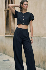 Pantalón de fit wide leg, cintura alta con pretina con detalle v posterior y trabillas, pinzas frontales, bolsillos delanteros, vivos decorativos posteriores, cierre frontal con botón en contraste y cremallera oculta.