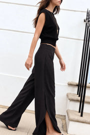Pantalón fluido de fit wide leg, cintura alta con pretina, pinzas frontales con detalle decorativo, bajo curveado asimétrico con olanes y detalle de abertura laterales. Cierre lateral con cremallera oculta.