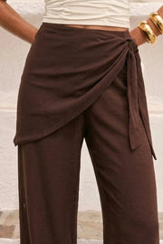 Pantalón fluido de fit recto, cintura media con pretina elástica, bolsillos delanteros y detalle de pareo decorativo con nudo lateral.
